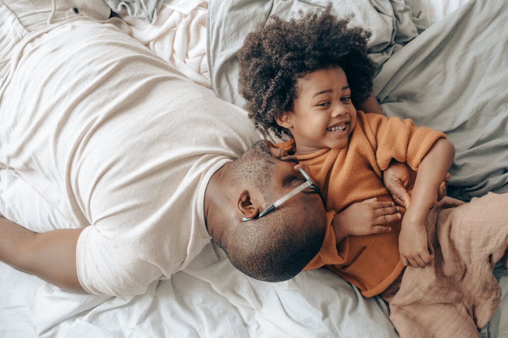 smiling african american dad and child on bed