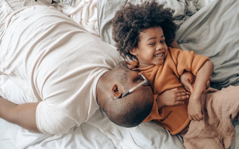 smiling african american dad and child on bed